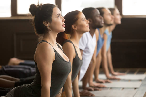 Group of sporty people in upward facing dog exercise Group of young sporty afro american and caucasian people practicing yoga lesson, stretching in upward facing dog exercise, Urdhva mukha shvanasana pose, working out, indoor close up, studio side view teenage yoga stock pictures, royalty-free photos & images