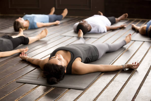 Group of sporty people in Savasana pose Group of young afro american and caucasian sporty people practicing yoga lesson lying in Dead Body pose, Savasana exercise, working out, resting after practice, indoor close up, studio yoga studio photos stock pictures, royalty-free photos & images