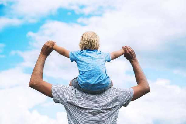 istock Father carrying his son on his back with raised arms up against the sky. 922362774