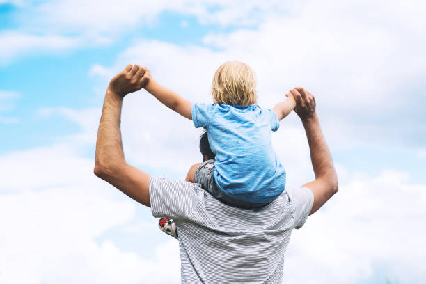 istock Father carrying his son on his back with raised arms up against the sky. 922363318