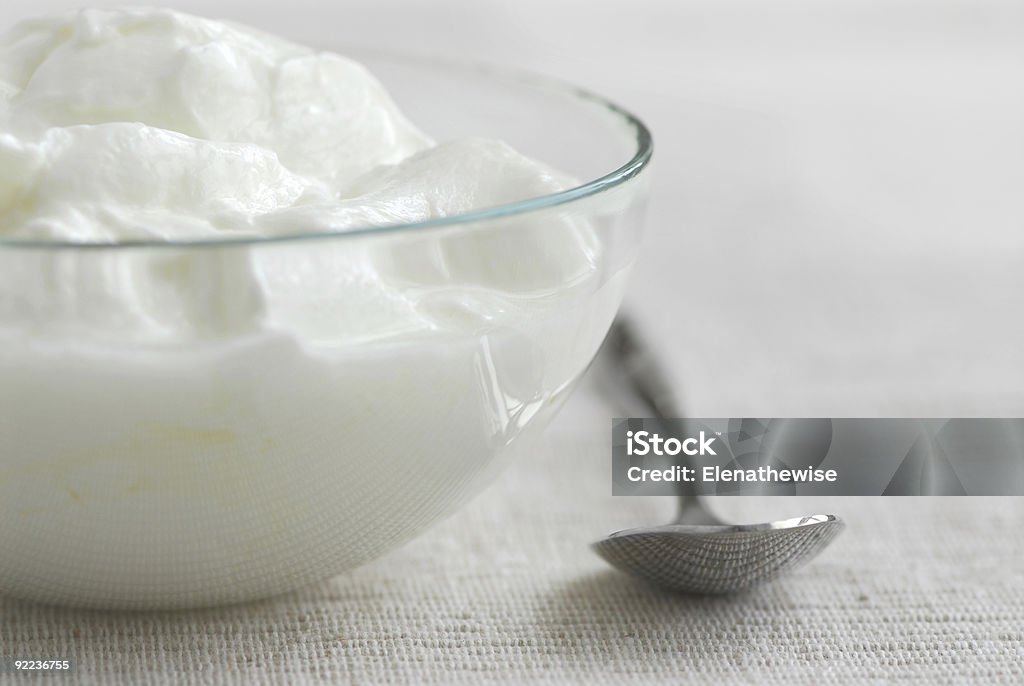 A close up photograph of a bowl of yogurt and a spoon Fresh yogurt served in a clear glass bowl Balance Stock Photo