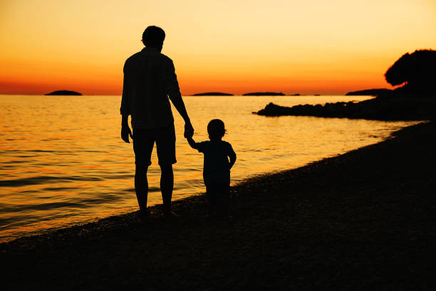 istock Father and son back silhouettes walking by the sea 922367870