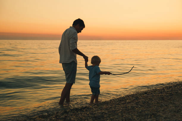 istock Father and son back silhouettes walking by the sea. 922367898