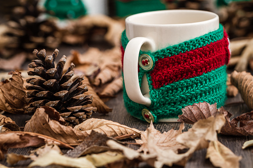 Mugs in knitted mittens, decorated for Christmas, on brown wooden background