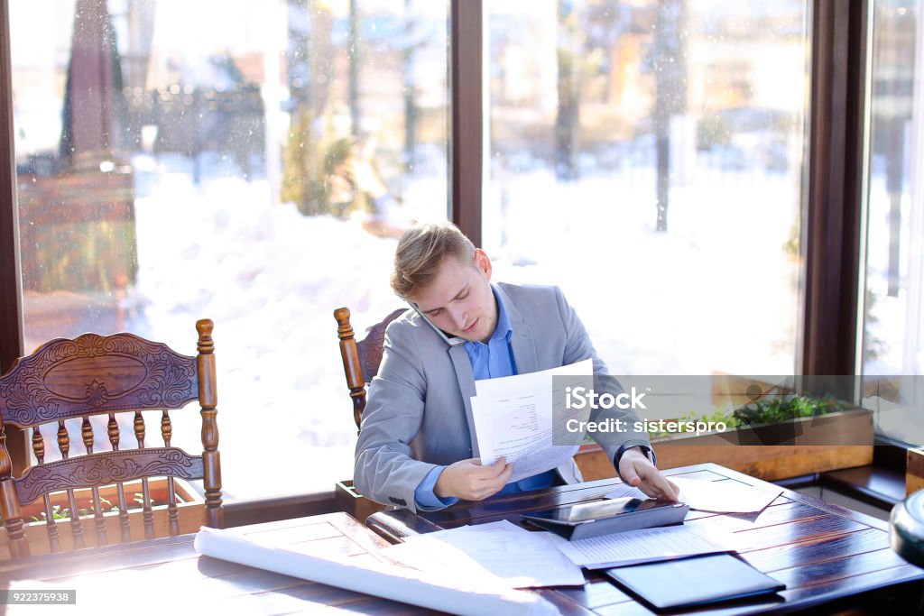 Young student preparing before exam in fast motion at cafe with Hardworking student preparing before exam in fast motion at cafe with papers and typing by tablet in fast motion. Young guy wears smart watch and grey suit. Concept of preparing before exam using gadgets and document. Adult Stock Photo