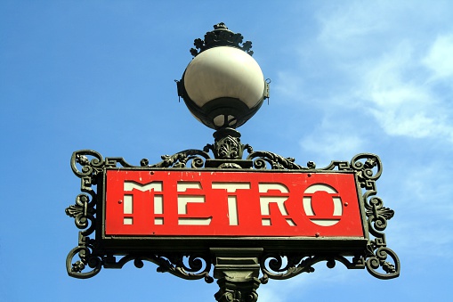 A metro sign for the Paris underground, with a light bulb on the top. Dusk. Blue sky in the background.