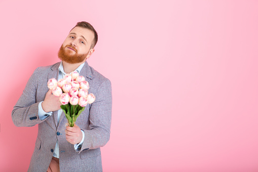 Handsome bearded man holding bouquet of tulips in hand on pink background. 8 march. copy space