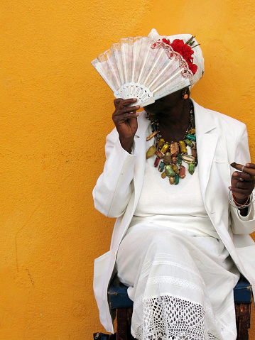 Portrait of senior afroamerican woman covering her face with traditional fan and a cuban cigar on the hand - taken on the streets of Havana