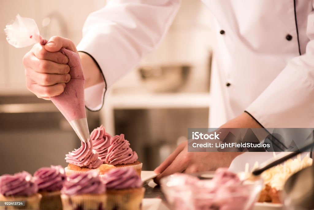 recadrée tir de confiseur, mettre la crème sur les cupcakes - Photo de Pâtissier libre de droits