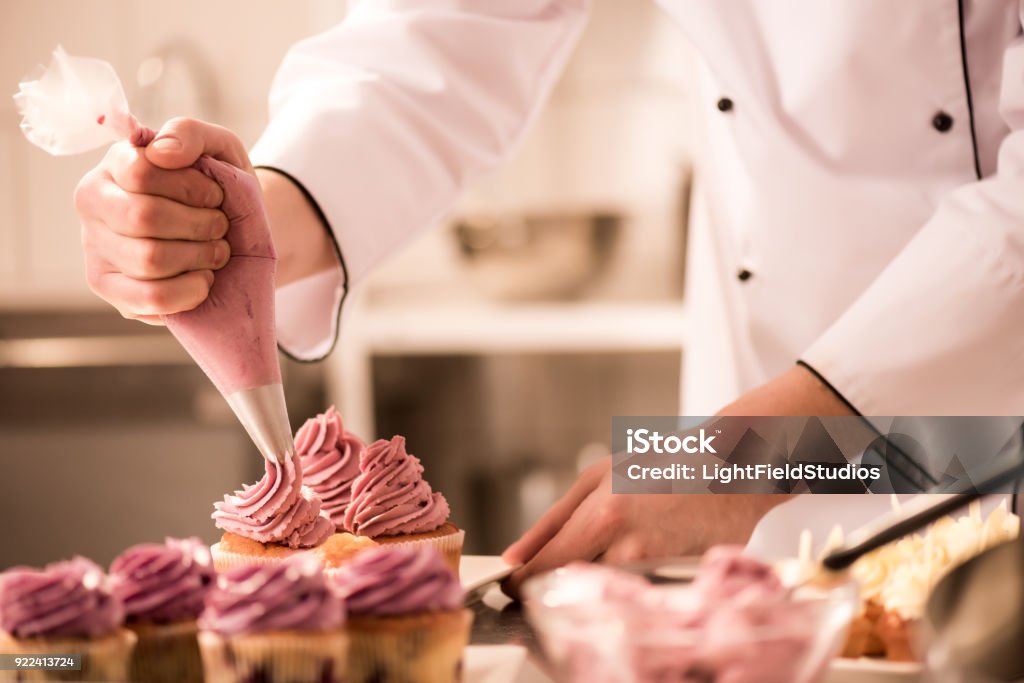 cropped shot of confectioner putting cream on cupcakes Confectioner Stock Photo