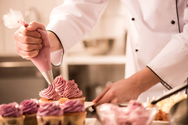 cropped shot of confectioner putting cream on cupcakes - cupcake cake sweet food dessert imagens e fotografias de stock