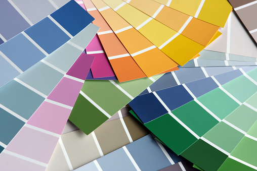 Choosing the right paint from colorful Paint Sample Color Swatch. The pant Sample Charts in variety of colors are spread over the table, the image is full frame close-up of the various color swatch.
