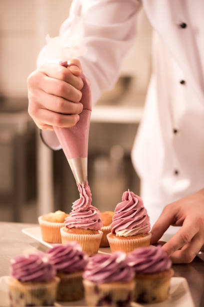 recadrée tir de confiseur, mettre la crème sur les cupcakes - pâtissier photos et images de collection