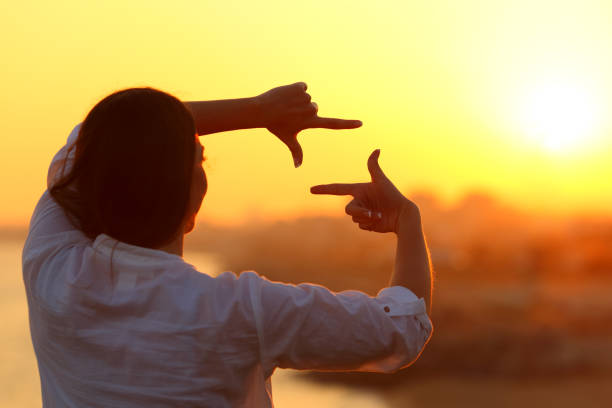 Woman framing with fingers at sunset Back view backlight portrait of a woman framing with fingers at sunset hand cropping photos stock pictures, royalty-free photos & images