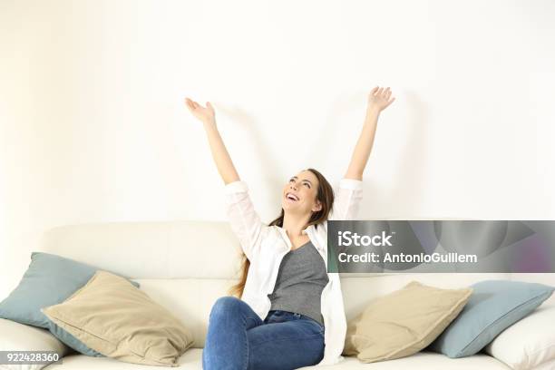 Happy Woman Raising Arms And Looking Above On A Couch Stock Photo - Download Image Now