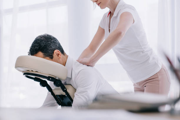 masseuse doing seated back massage for businessman at office stock photo
