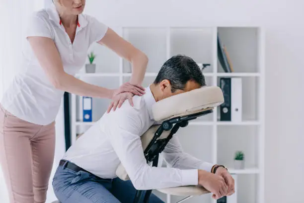 Photo of beautiful adult masseuse doing seated massage for businessman