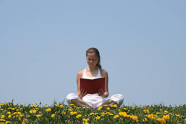 Young woman reading a book in flowering meadow
