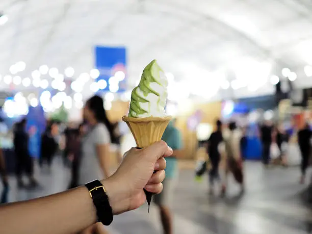 Photo of Woman's hand holds soft served ice cream vanilla and green tea 2 tone flavored in wafer cone.