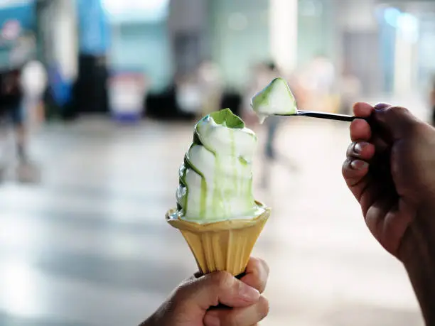 Photo of Woman's hand holds soft served ice cream vanilla and green tea 2 tone flavored in wafer cone.