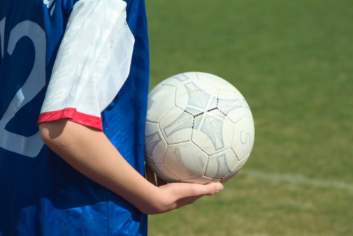 Smiling Mixed raced  8 years old girl wearing blue soccer uniform sitting at soccer grass field.