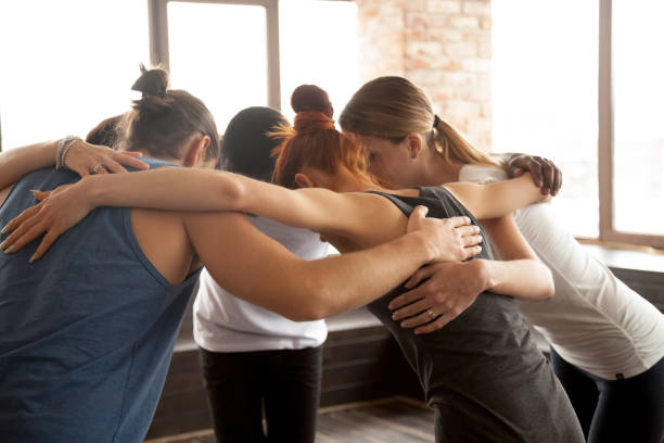 Young people embracing in circle standing together, group unity concept Young diverse people embracing uniting in circle standing together indoors, multiracial team of black and white friends hugging promising help support in common goal achievement, group unity concept teen yoga stock pictures, royalty-free photos & images