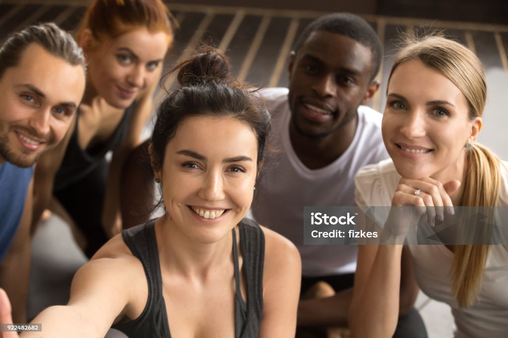 Sporty multiracial friends taking group selfie holding looking at camera Young smiling sporty multiracial friends taking group selfie photo holding looking at camera, happy healthy diverse fit people making self-portrait after working out together in gym, view from camera Variation Stock Photo