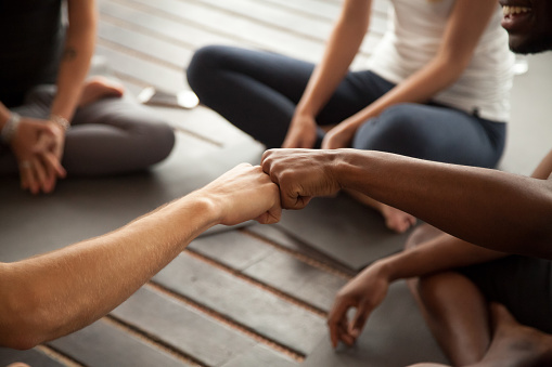 African and caucasian men fist bumping at group meeting in gym studio, two multiracial black and white friends greeting with friendly gesture celebrating team training teamwork, hands close up view