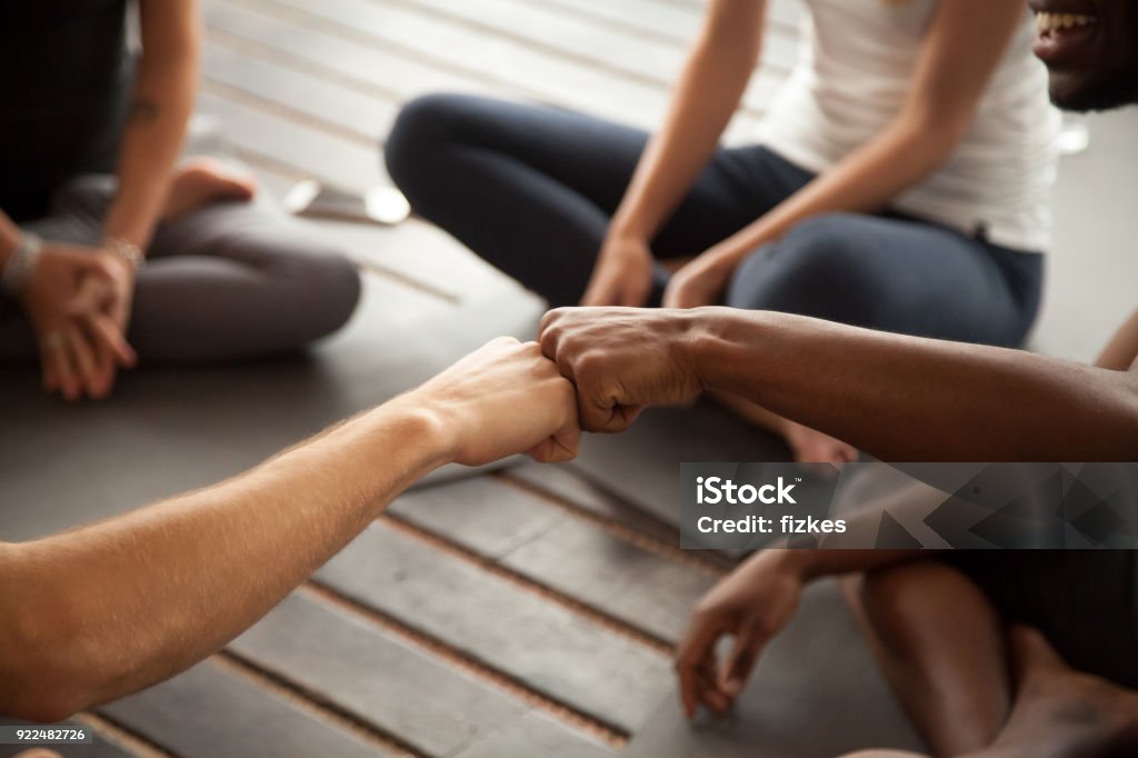 African and caucasian men fist bumping at group meeting, closeup African and caucasian men fist bumping at group meeting in gym studio, two multiracial black and white friends greeting with friendly gesture celebrating team training teamwork, hands close up view Wellbeing Stock Photo