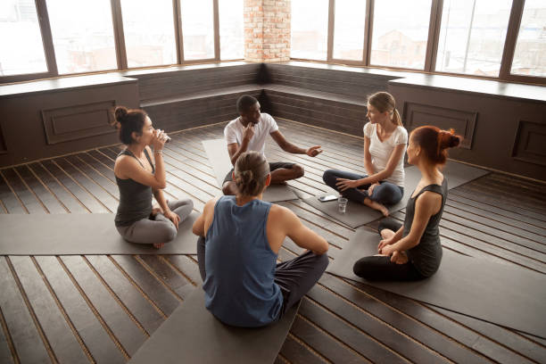istruttore di yoga afro-americano che parla con diversi gruppi seduti sul tappetino - yoga meeting foto e immagini stock