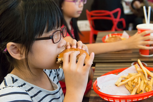 Little Asian girl eating a hamburger and french fries in the restaurant