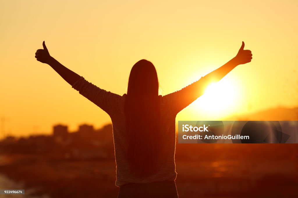 Luz de fondo de una mujer levantando los brazos con pulgares - Foto de stock de Emoción positiva libre de derechos