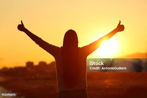 Backlight Of A Woman Raising Arms With Thumbs Up Stock Photo - Download Image Now - Positive Emotion, Confidence, Attitude