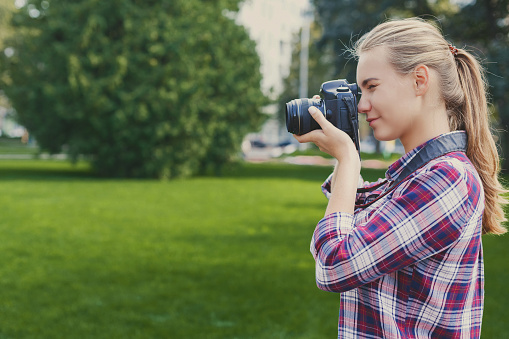 Attractive young woman photographing with professional camera outdoors, copy space. Taking photos and photography classes concept