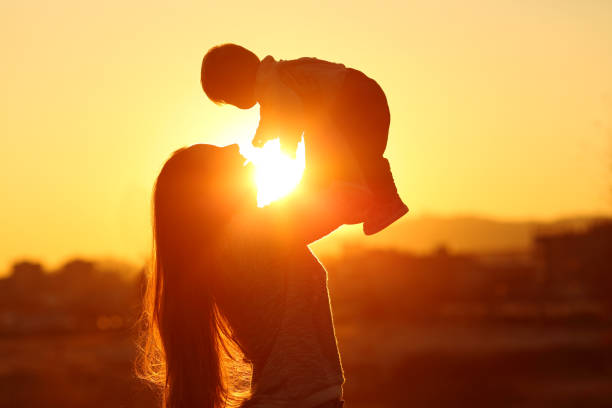 mère d’élever son fils enfant au coucher du soleil avec le soleil au milieu - female nurse photos et images de collection