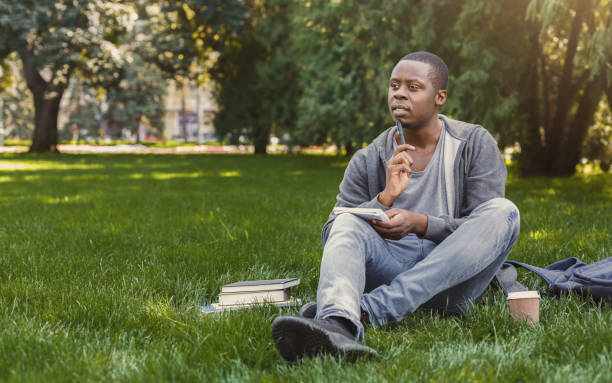 istock Concentrated african-american studen sitting with notebook on grass 922505968