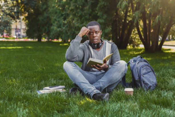istock Desperate african-american student reading book in campus on grass 922506058