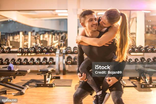 Schönen Jungen Mann Auf Seine Freundin In Der Turnhalle Huckepack Tragen Stockfoto und mehr Bilder von Trainingsraum - Freizeiteinrichtung