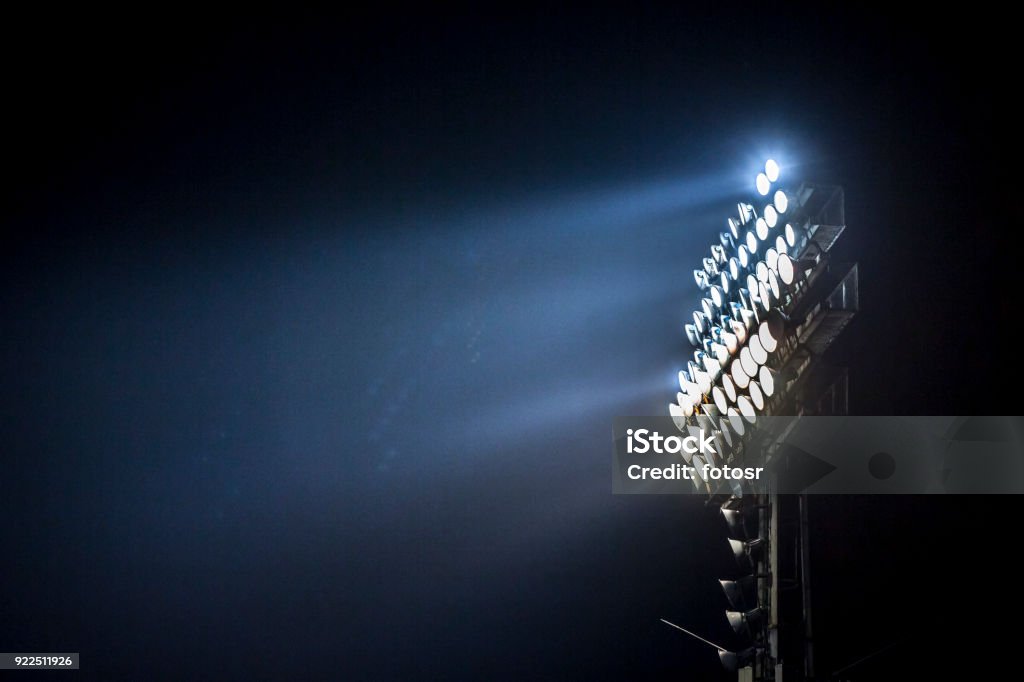 Light tower lit at a stadium during nightime. Light tower lit at a stadium during nightime.Light tower lit at a stadium during nightime. American Football - Sport Stock Photo