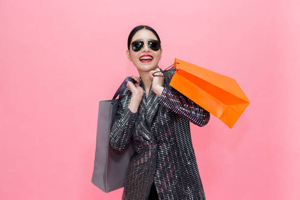 young stylish asian woman carrying shopping bags and holding credit card. beautiful fashionable woman with sunglasses isolated over pink background. shopping and finance concept - asian ethnicity fashion model beautiful luxury imagens e fotografias de stock