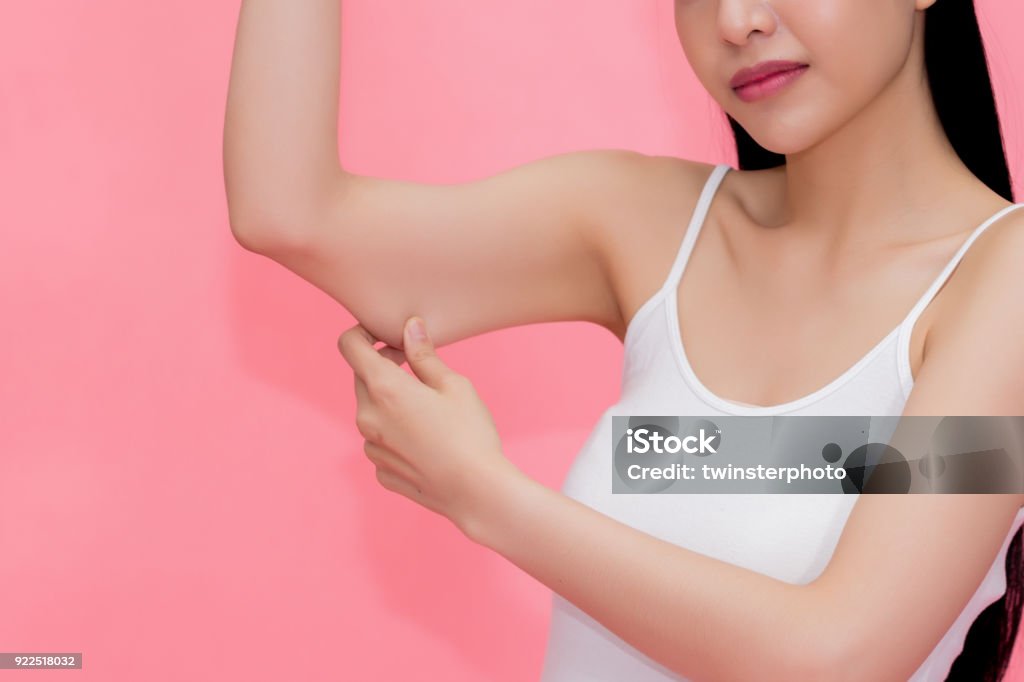 Young attractive Asian woman pinching excess fat and cellulite in her upper arms as she lacks exercise and healthy lifestyle. Young attractive Asian woman pinching excess fat and cellulite in her upper arms as she lacks exercise and healthy lifestyle Arm Stock Photo