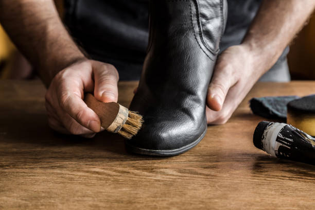 Man's hand cleaning elegant leather boots with brush. Cares about boots beauty and protection from cold and wet. Preparing for autumn and winter season. Footwear cleaning concept. Man's hand cleaning elegant leather boots with brush. Cares about boots beauty and protection from cold and wet. Preparing for autumn and winter season. Footwear cleaning concept. shoe polish photos stock pictures, royalty-free photos & images