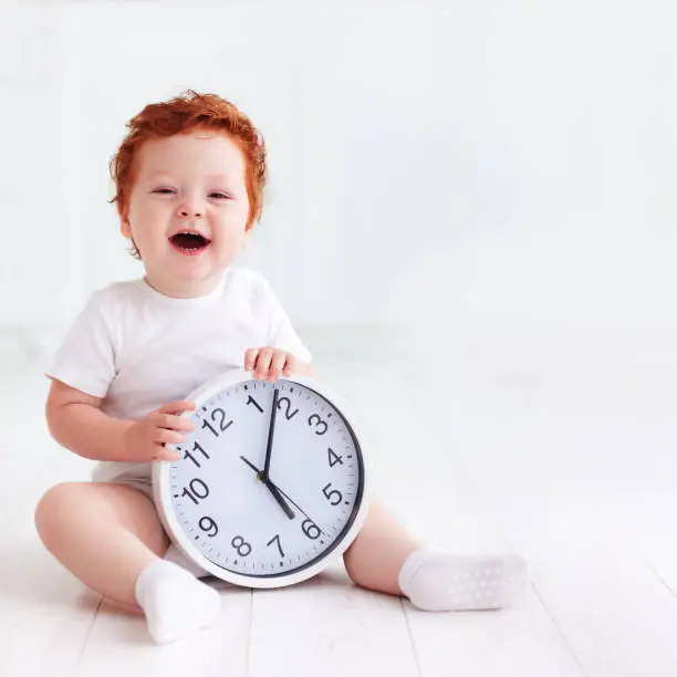 Photo of happy little toddler baby holding circle clock