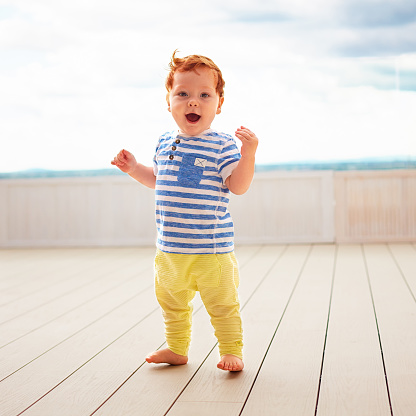 portrait of cute redhead, one year old baby boy walking on decking