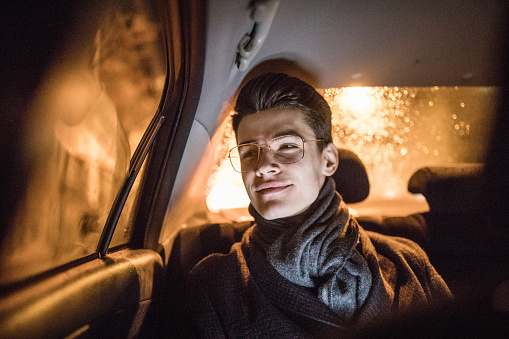 Young man sitting on the backseat of the car and enjoys driving through the city at night