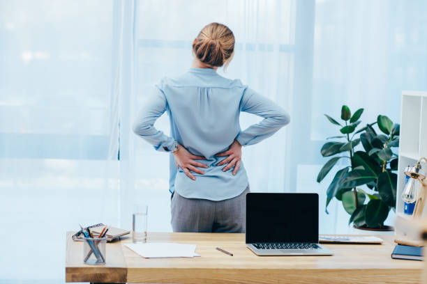 vista posteriore di imprenditrice con backplain in ufficio - back rear view pain backache foto e immagini stock