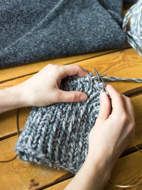 istock Crafting scene: woman knits a gray hat on wooden table using knitting needles 922543446