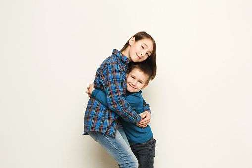 Portrait of happy hugging brother and sister, white studio background. Cute girl and boy embracing, smiling at camera, copy space