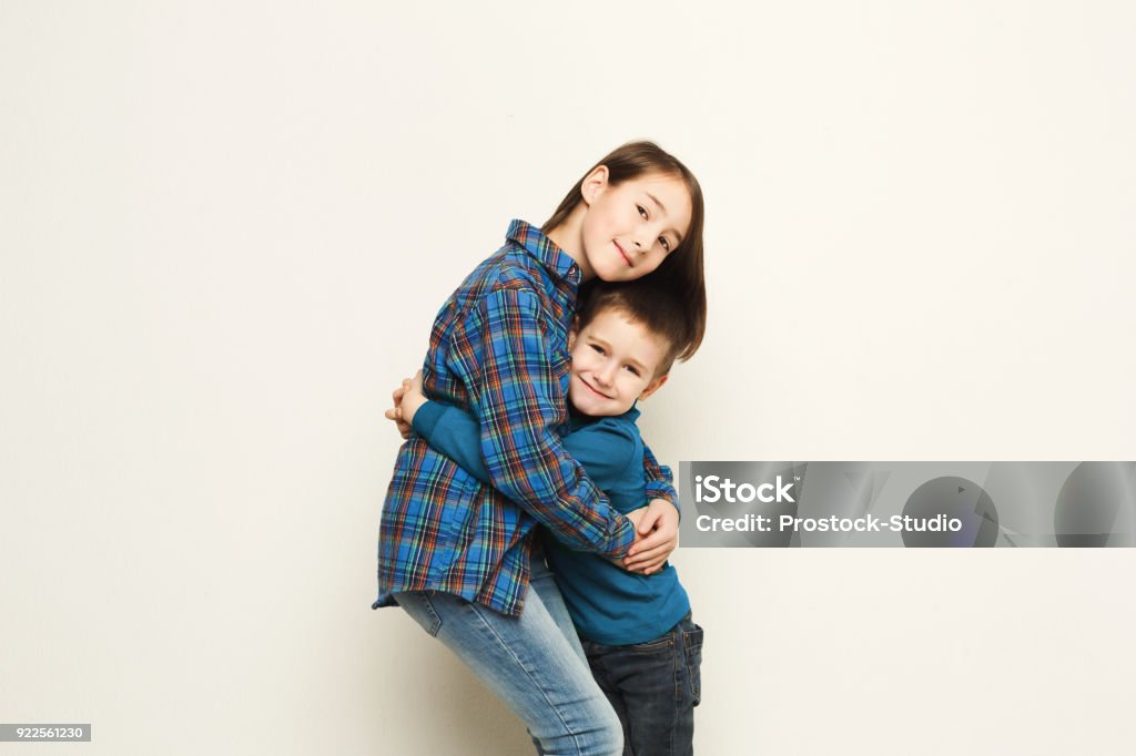 Happy brother and sister hug, studio background Portrait of happy hugging brother and sister, white studio background. Cute girl and boy embracing, smiling at camera, copy space Brother Stock Photo