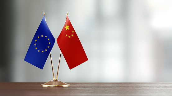 European Union and Chinese flag pair on desk over defocused background. Horizontal composition with copy space and selective focus.